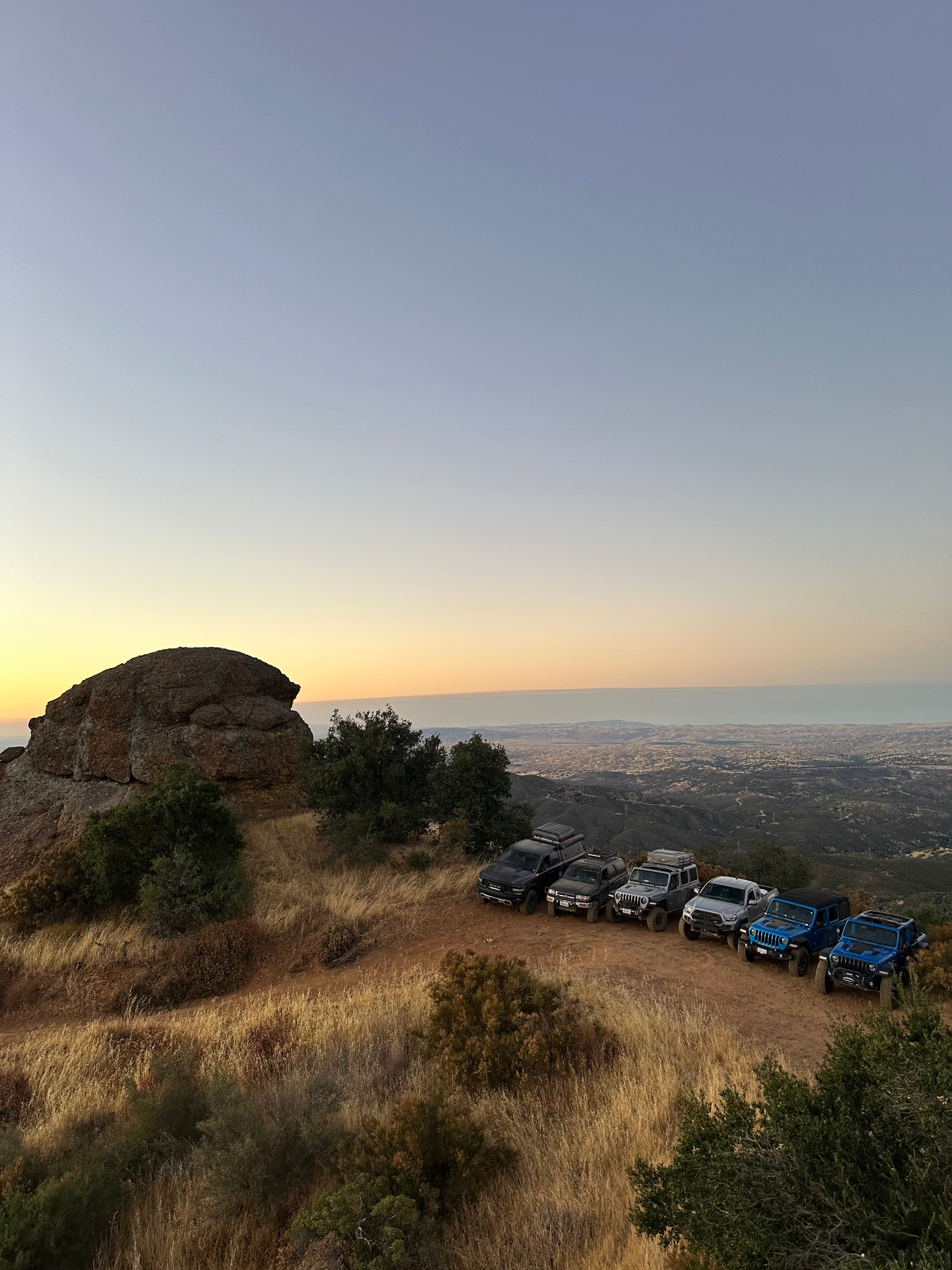 Line of offroad rigs parked at sunset on a ridge above the Central Coast