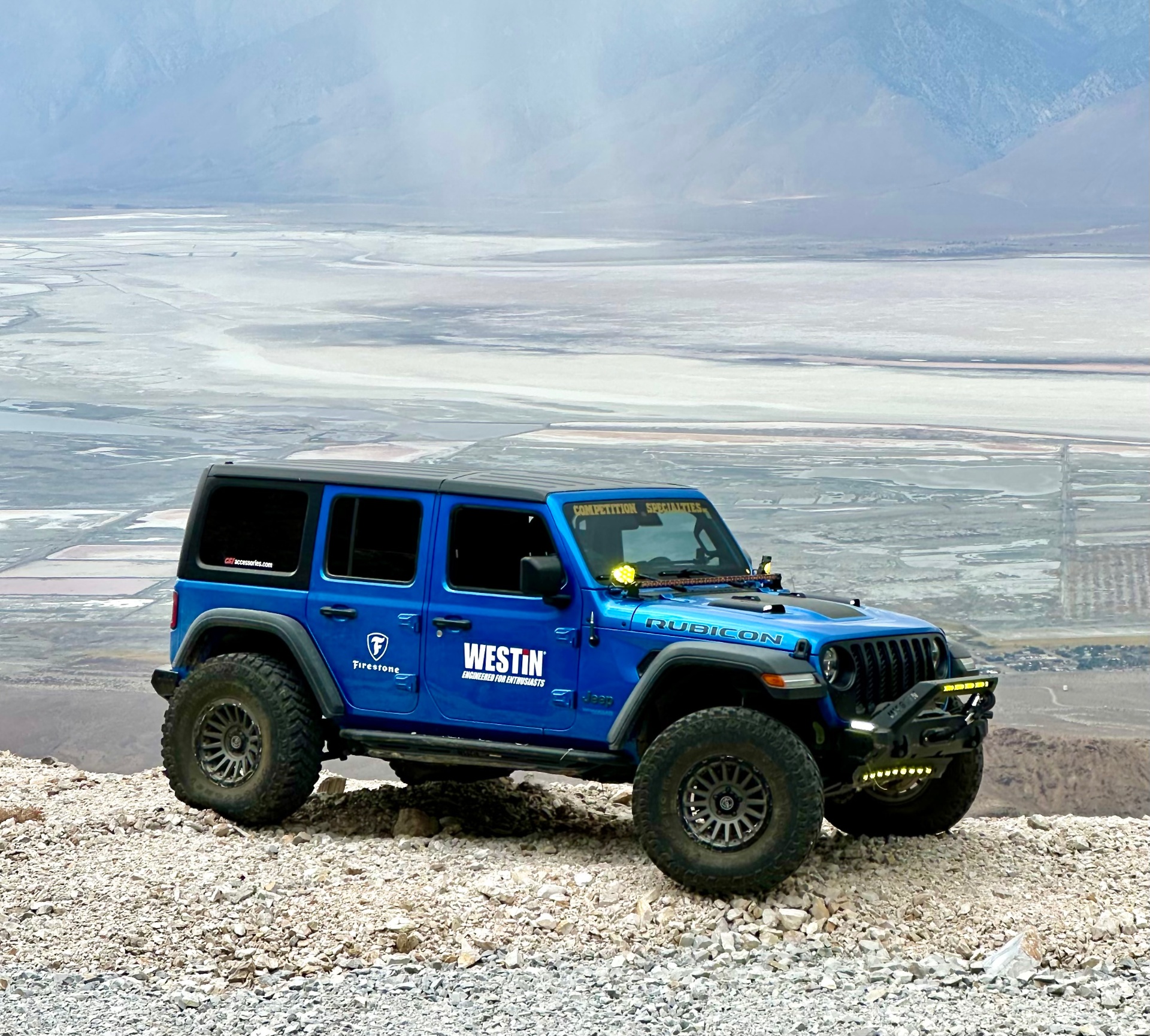 Blue Westin Jeep parked on a rocky overlook above a pale desert basin